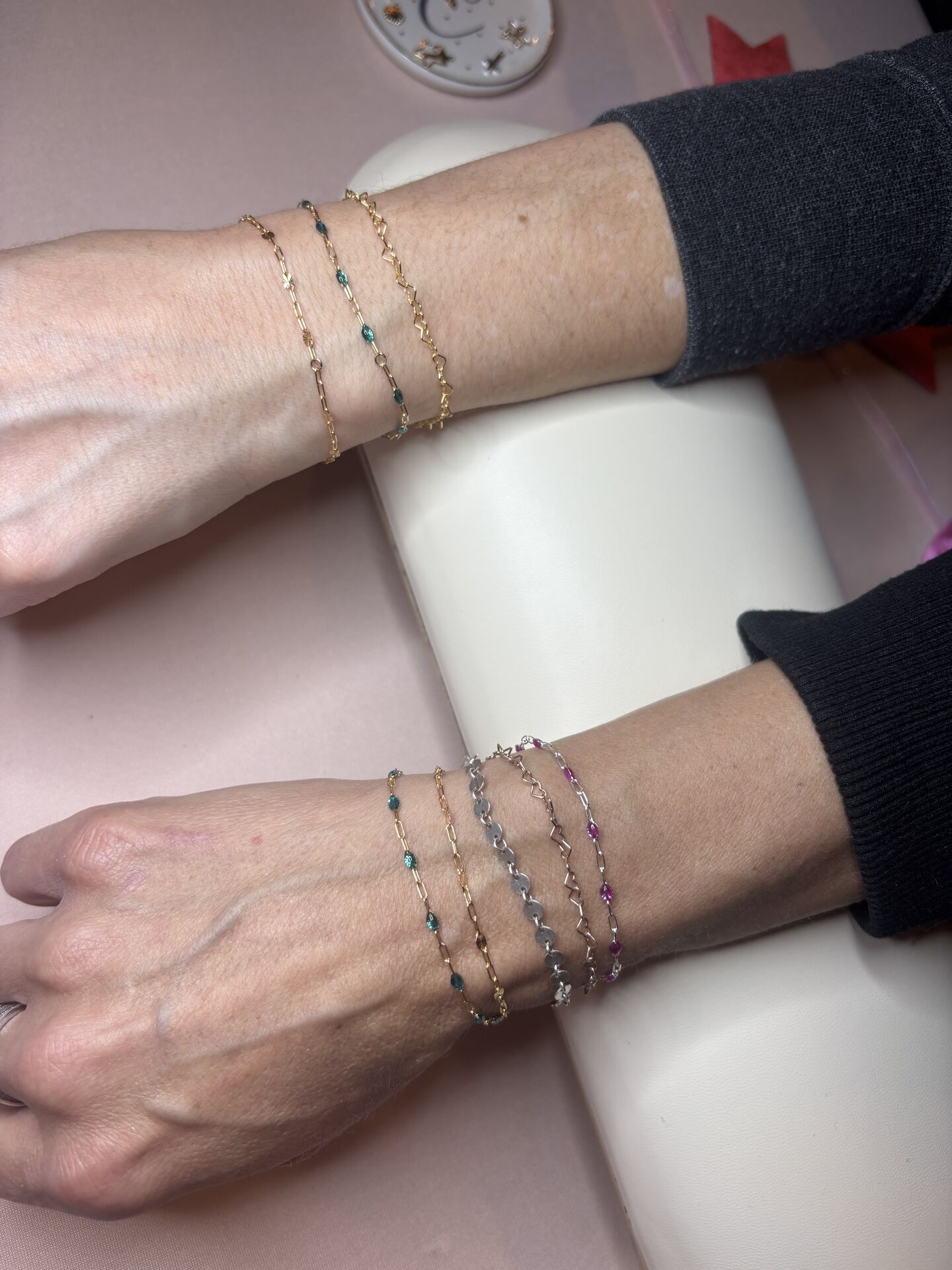 Two wrists wearing layered gold and colorful permanent bracelets