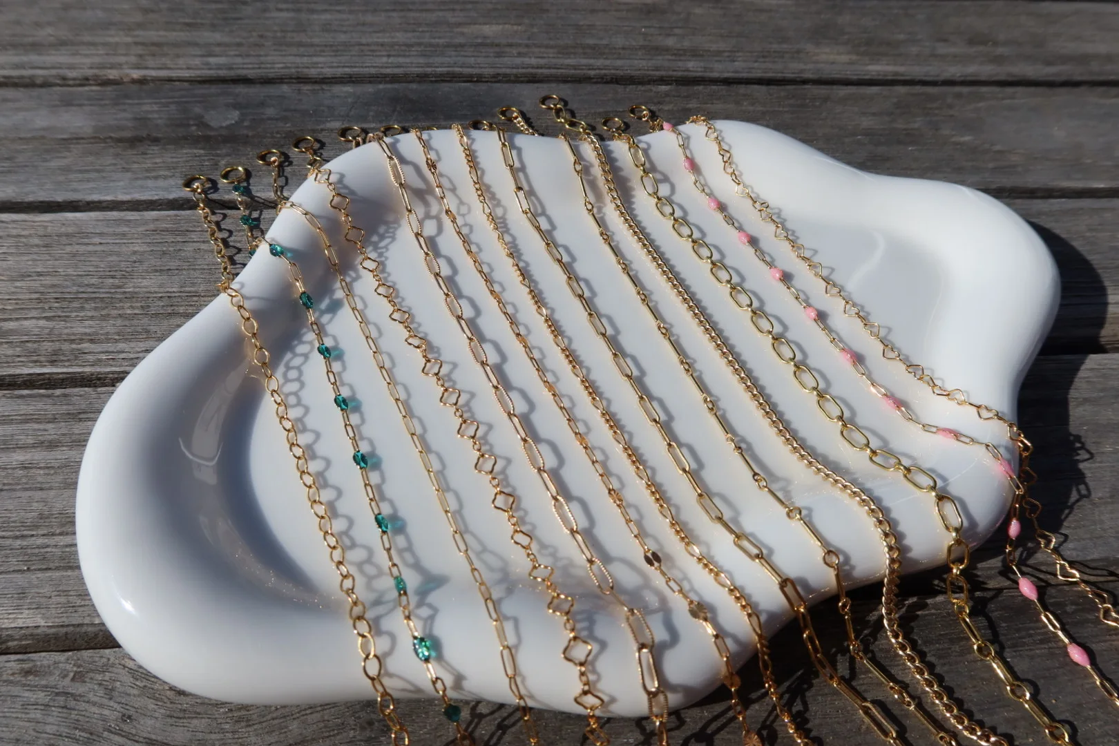 Gold-filled permanent jewelry chains draped across a white display tray