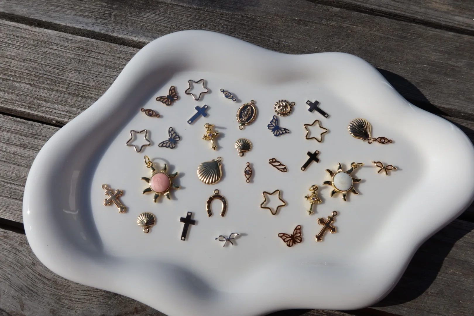 Permanent jewelry charms including stars, shells, butterflies, and celestial shapes